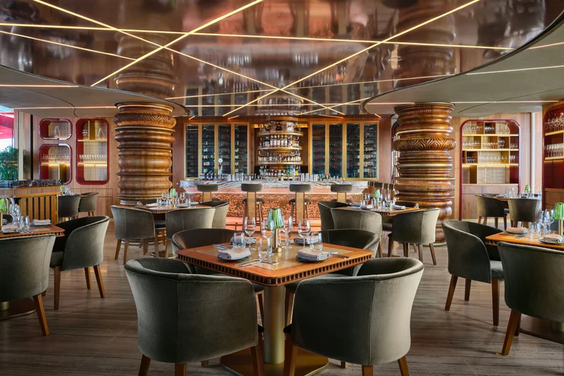Ce La Vi rooftop restaurant interior with emerald velvet seating, bronze sculptural columns, and geometric mirrored ceiling with golden lighting